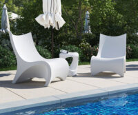 Two white lounge chairs next to a pool.